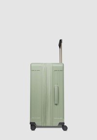 Maleta rígida en color verde claro, con una superficie texturizada, dos ruedas, un mango telescópico y líneas de acento verticales en los laterales.