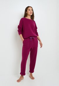 Sweatshirt fuchsia avec un col bateau et des manches droites associé à un jogging coordonné avec un cordon de serrage et des poignets roulés.