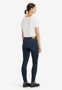 Vaqueros ajustados de color azul oscuro con icónicos bolsillos traseros, combinados con una camiseta blanca de manga corta. Calzado negro completa el conjunto.