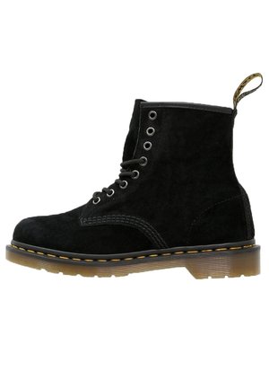 Botte de chelsea en suède noir à lacets, avec des coutures jaunes, une semelle translucide marron et une languette en tissu à l'arrière.