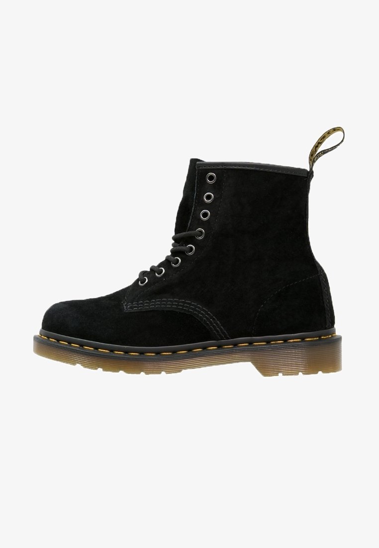 Botín de ante negro con cordones, costuras amarillas, suela translúcida marrón y tira de tela en la parte trasera.