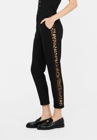 Pantaloni neri con una striscia laterale a stampa leopardo, realizzati in un tessuto morbido, con tasche e orlo risvoltato. Abbinati a eleganti mocassini neri.