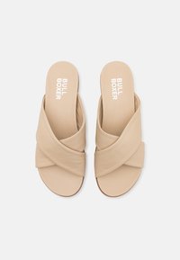 Sandali infradito beige con design a incrocio, realizzati in materiale morbido, con una texture liscia e suola piatta, logo in rilievo sulla soletta.