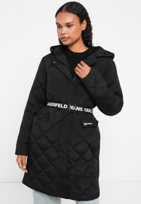 Cappotto imbottito nero con cappuccio, caratterizzato da una vita con cintura e logo, tasche frontali e tessuto testurizzato. Ideale per il clima freddo.