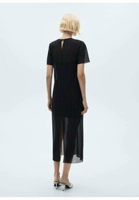 Črna obleka do kolen s kratkimi rokavi, z teksturirano, naborkano zasnovo in odprtino na hrbtu. Stranski razporek za lažje gibanje.