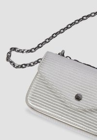 Mała srebrna torebka crossbody o teksturowanej powierzchni, z klapą i magnetycznym zapięciem, z czarnym metalowym łańcuszkiem na jasnym tle.