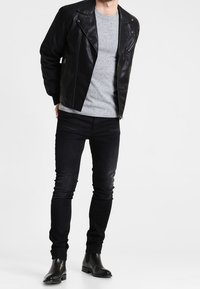 Giubbino in pelle nera da motociclista, maglione grigio a maglia, jeans skinny neri e stivaletti Chelsea neri. Il giubbotto presenta dettagli con zip e un design strutturato.