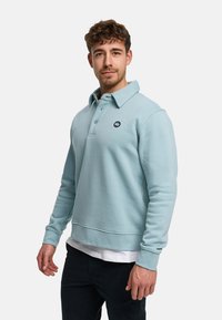 Lyseblå bomulds polo-sweater med opbrettet krave, tre-knaps lukning og et logo på brystet. Har ribstrikkede manchetter og kant.