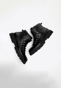 Czarne skórzane buty trekkingowe o teksturze, z metalowymi oczkami, grubą gumową podeszwą oraz wyściółką wokół kostki dla lepszego wsparcia.