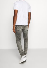Camiseta blanca de manga corta, jeans ajustados grises con efecto desgastado y zapatillas blancas. Conjunto simple y casual con un diseño minimalista.