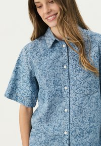 Kurzarm-Hemd in Hellblau mit floralem Muster, ausgestattet mit einem Kragen und einer linken Brusttasche. Hergestellt aus strukturiertem Stoff.