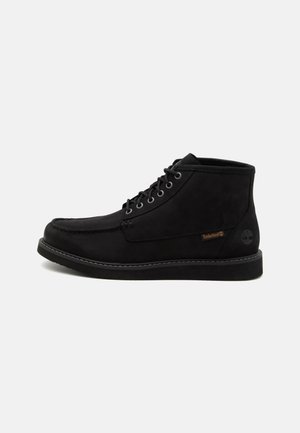 Sorte ruskinds ankelstøvler med metaløjer, matchende snørebånd, en kontrasterende sål og et Timberland-logo på siden. Glat tekstur.
