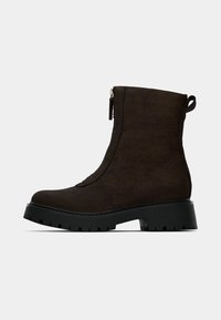 Dark brown suede ankle boot with black chunky sole, side zipper, and pull tab on a plain white background.