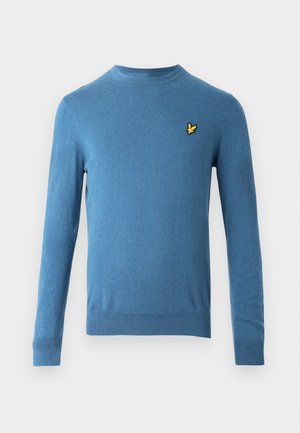 Plavi pleteni džemper s dugim rukavima, okruglim izrezom i malim žutim logom ptice na lijevoj strani prsa. Glatka tekstura i uski kroj.