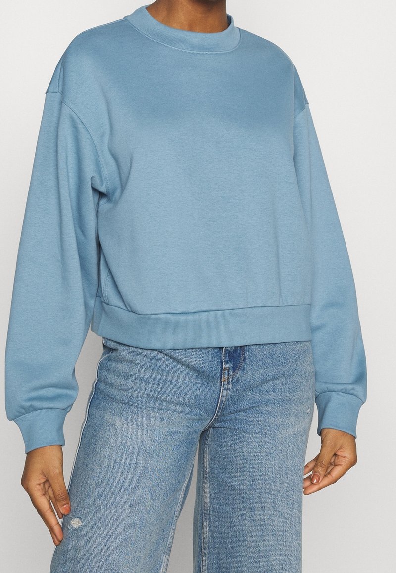 Sweat-shirt bleu clair en coton doux, avec un col rond, des manches longues et une coupe courte. Associé à un jean en denim délavé pour compléter le look.