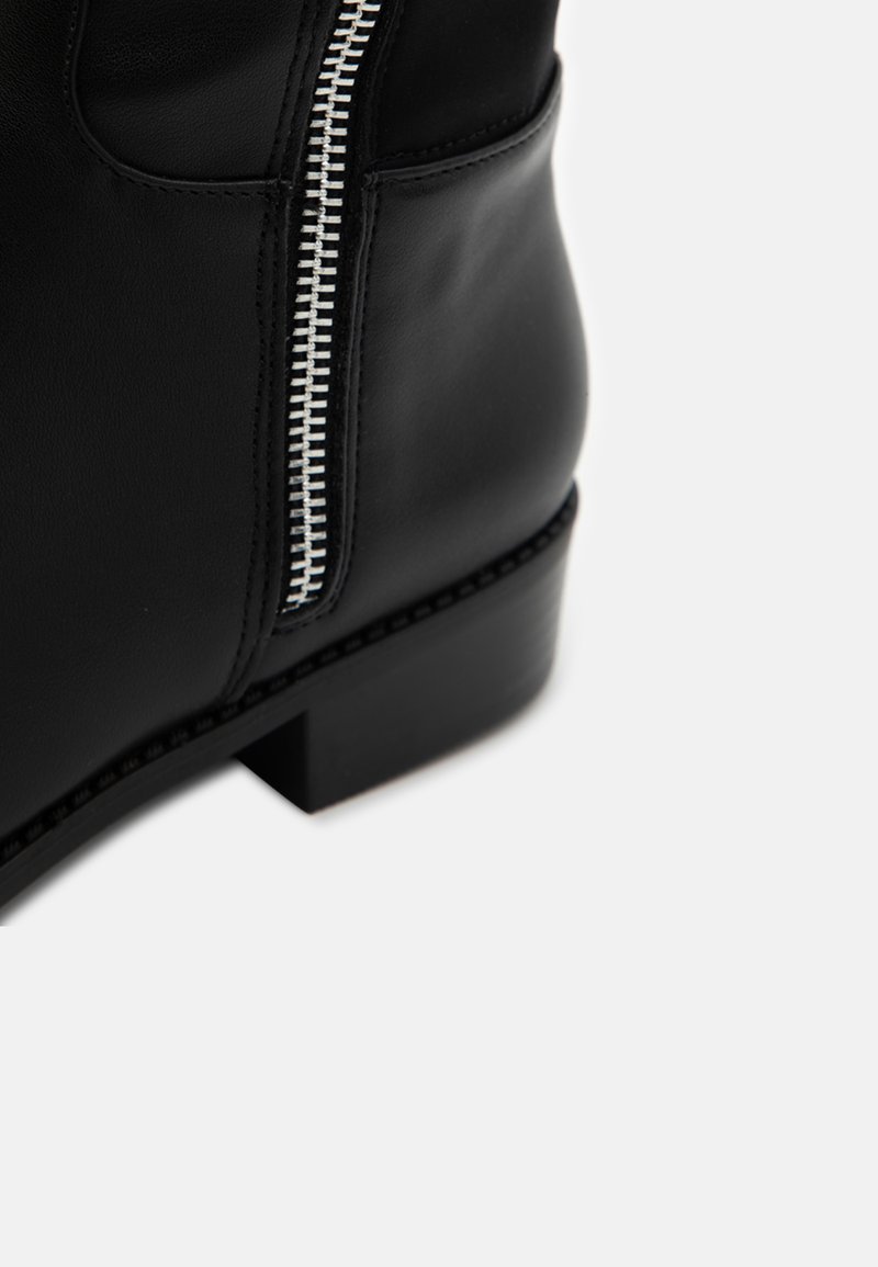 Zwarte leren enkelboot met een rits aan de zijkant, platte hak en gestikte details langs de zool. Glad materiaal met een slanke uitstraling.