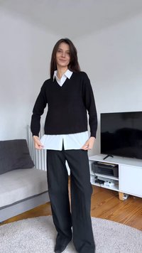 Μαύρο πλεκτό πουλόβερ φορεμένο πάνω από λευκό πουκάμισο με γιακά, συνδυασμένο με μαύρο παντελόνι φαρδιάς γραμμής. Απλός σχεδιασμός, άνετη εφαρμογή και αντιθετικά χρώματα.