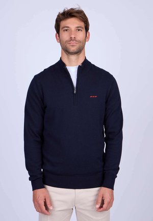 Pull-over en tricot bleu marine à fermeture zip mi-hauteur, avec une finition texturée et un accent logo rouge sur la poitrine. Poignets et ourlet côtelés.