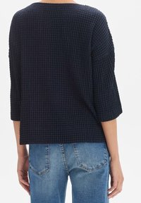 Mörkblå tröja med strukturerad, våffelstickad mönster, ¾-ärmar och avspänt snitt, kombinerad med ljusblå jeans.