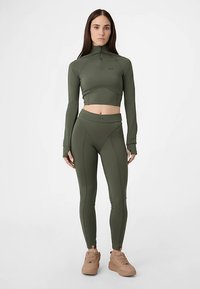 Olivgrünes sportliches Crop-Top mit hohem Kragen und langen Ärmeln, kombiniert mit passenden, hochtaillierten Leggings mit Nahtdetails.