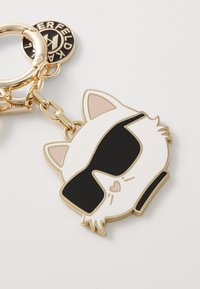 Portachiavi dorato con un design a forma di faccia di gatto, occhiali da sole neri, accenti rosa sulle orecchie e superficie lucida, attaccato tramite una catena.