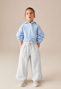 Lysblå hættetrøje med elastisk talje og optrukne ærmer, kombineret med lysegrå oversized sweatpants og beige sneakers.