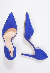 Modré semišové lodičky na vysokém podpatku s špičatými špičkami a vykrojenými stranami. Úzké stiletto podpatky a hladká vnitřní podšívka.