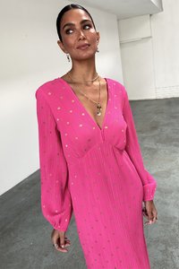 Pink dress with textured pleats and gold foil accents, featuring a deep V-neck and long sleeves. Simple jewelry complements the outfit.