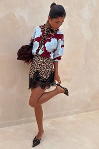 Πλεκτό πουλόβερ με κόκκινα και μπλε λουλουδένια σχέδια, συνδυασμένο με φούστα λεοπάρ σχέδιο με μαύρη δαντέλα στο τελείωμα. Παπούτσια με μυτερό μυτάκι και διακοσμητικά στοιχεία.