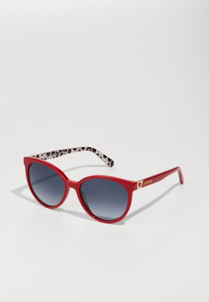 Red cat-eye sunglasses with gradient gray lenses, featuring a bold frame and patterned black and white temple arms. Accented with gold hardware.