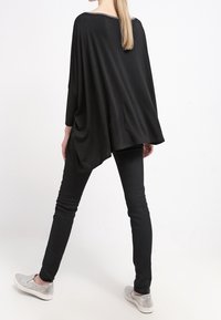 Svart överdimensionerad topp med rundad halsringning och fladdermusärmar, tillsammans med svarta slim-fit jeans och gråa slip-on skor.