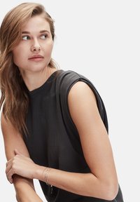 Top nero senza maniche realizzato in morbido tessuto, con una texture liscia e un design delle spalle arrotondato. Braccialetti d'argento al polso aggiungono un tocco di dettaglio.