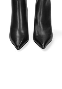 Bottes noires en cuir à talons hauts avec un bout pointu. Texture lisse, design élégant et talon aigu. Style minimaliste sans accents matériels.