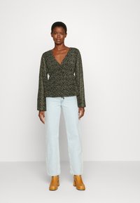 Top envolvente com estampado floral verde e mangas compridas, combinado com jeans de estilo vintage em azul claro e botas de cano curto de salto alto em tom bege.