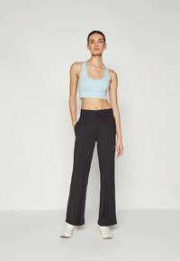 Svetlomodrý skrátený top a čierne široké nohavice. Tkanina vyzerá mäkko s hladkou textúrou. Biele športové topánky dopĺňajú vzhľad.