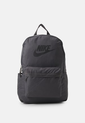 Mochila negra de Nike con bolsillo frontal con cremallera, asa superior y gran logo de Nike en el compartimento principal sobre un fondo blanco liso.