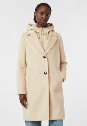 Beige wool-blend coat with large lapels, a single button closure, and two side pockets, layered over a light padded hoodie.