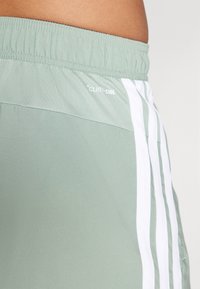 Helle grüne Sportshorts mit einem dehnbaren Taillenbund, die weiße Streifen an den Seiten und ein sichtbares "CLIMACOOL"-Logo aufweisen.