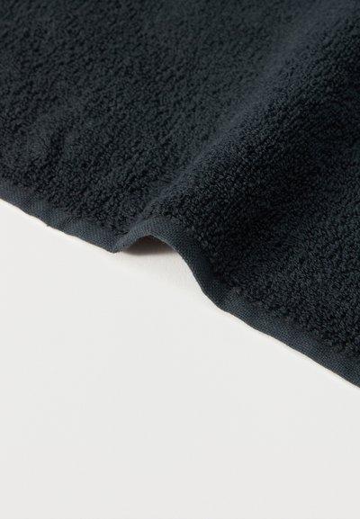 Σκούρο γκρι υφασμάτινη υφή με απαλή επιφάνεια πετσέτας, διπλωμένη πάνω σε ανοιχτό φόντο, εμφανίζοντας το πάχος και τις άκρες της.