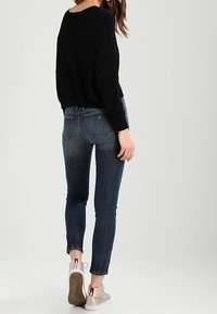 Černý oversize svetr, tmavě modré skinny džíny s vybledlými detaily a béžové tenisky. Džíny mají pět kapsičkový design a vyšívané akcenty.