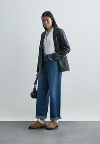 Μαύρο δερμάτινο σακάκι, λευκή ριγέ μπλούζα, τζιν ψηλόμεσο μπλε, φαρδιά γραμμή, καφέ παπούτσια επενδεδυμένα με γούνα, κρατώντας μια μικρή μαύρη τσάντα.