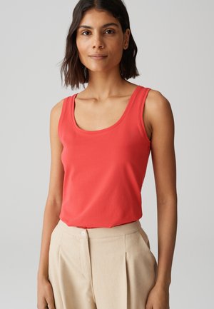 Koraalkleurige tanktop met een ronde hals en brede bandjes, gemaakt van zachte stof; gecombineerd met lichtbeige op maat gemaakte broek met een knoopsluiting.