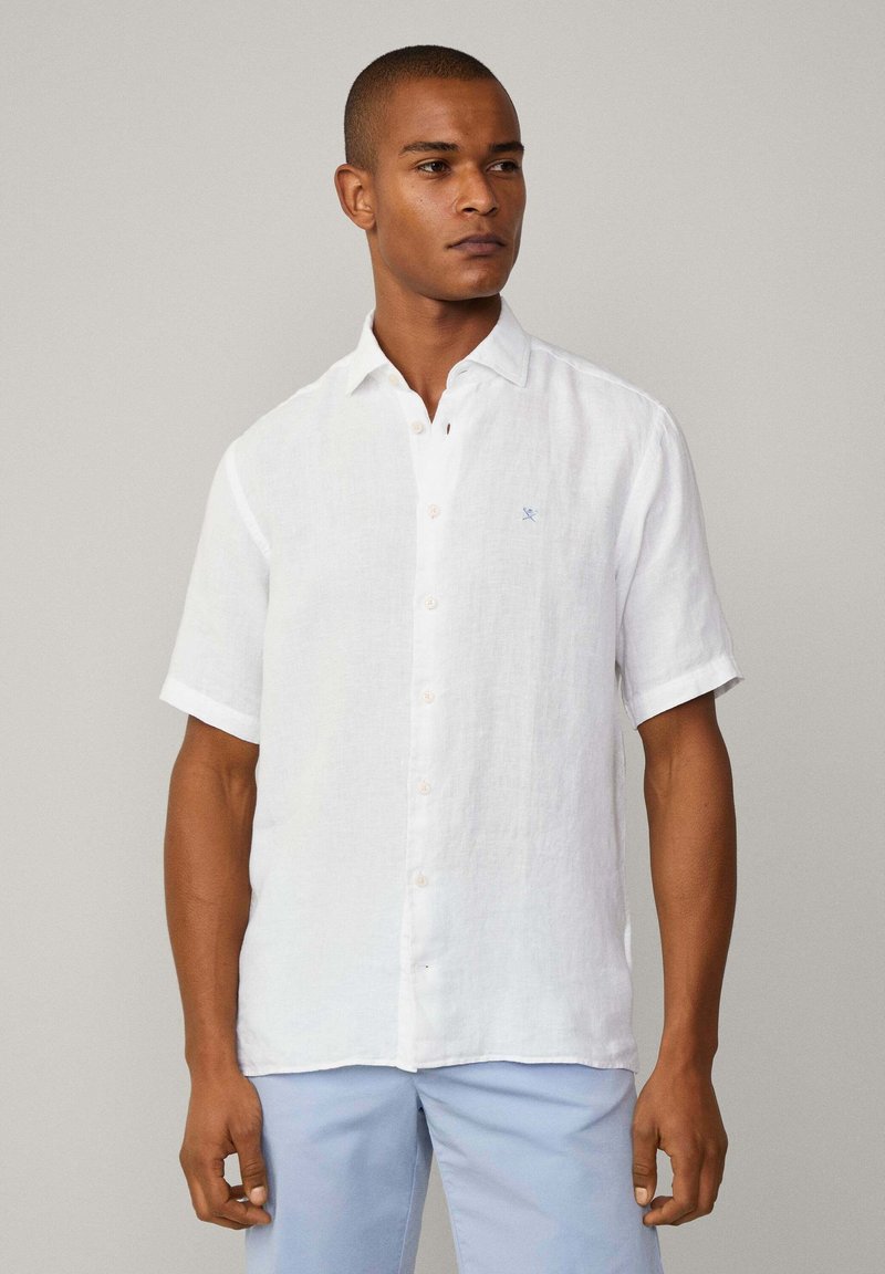 White linen short-sleeve shirt with a button-down collar, beige buttons, and small blue logo on the chest. Smooth texture, relaxed fit.
