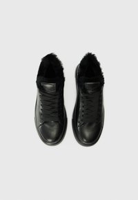 Baskets en cuir noir avec un col en fourrure, présentant un bout arrondi, des lacets noirs plats et une texture lisse sur l'ensemble.
