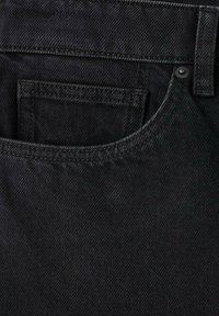 Detailný záber na vrecko čiernych džínsov z denimu so zreteľným prešívaním, očkom na opasok a detailom kovového nitovania.