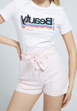Woman wearing a white t-shirt with colorful "Beauty" text and high-waisted light pink shorts tied with a bow at the waist.
