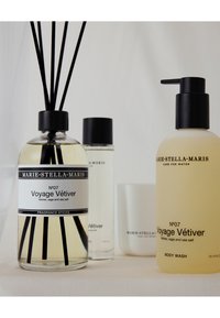 Trois produits Marie-Stella-Maris : un diffuseur de parfum en verre clair avec des bâtonnets noirs, une bouteille transparente et un gel douche jaune avec pompe.