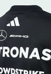 Černý sportovní dres s bílým textem a logy: "PETRONAS", "CROWDSTRIKE" a emblemů značek. Vyrobeno z hladké, lehké tkaniny.
