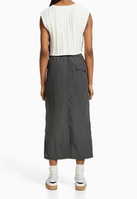 Grauer knielanger Rock mit strukturierter, plissierter Optik und einer Seitentasche, kombiniert mit einem gestrickten, ärmellosen Top in Cremefarben.