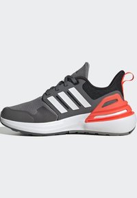 Zapatilla deportiva gris con rayas blancas, parte superior de malla, acentos texturizados y detalle rojo en el talón. Diseño ligero con lengüeta acolchada.
